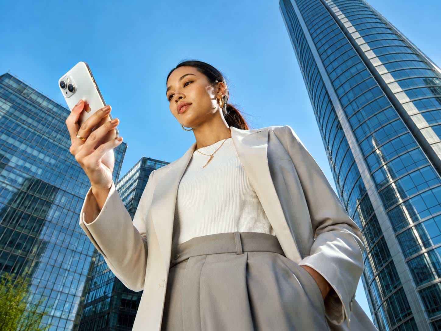 Woman checking an iPhone outside glass office towers